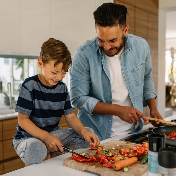 Little boy cutting vegetables while his father cooking food in kitchen.