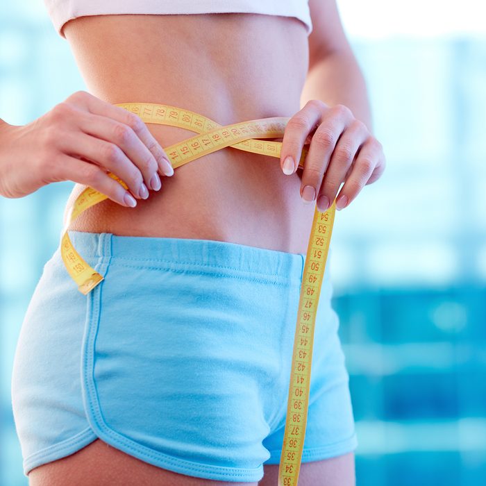 Close-up of a woman in sportswear measuring her waist