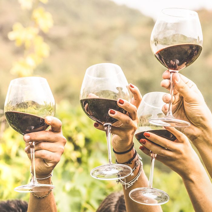 Hands toasting red wine glass and friends having fun cheering at winetasting experience