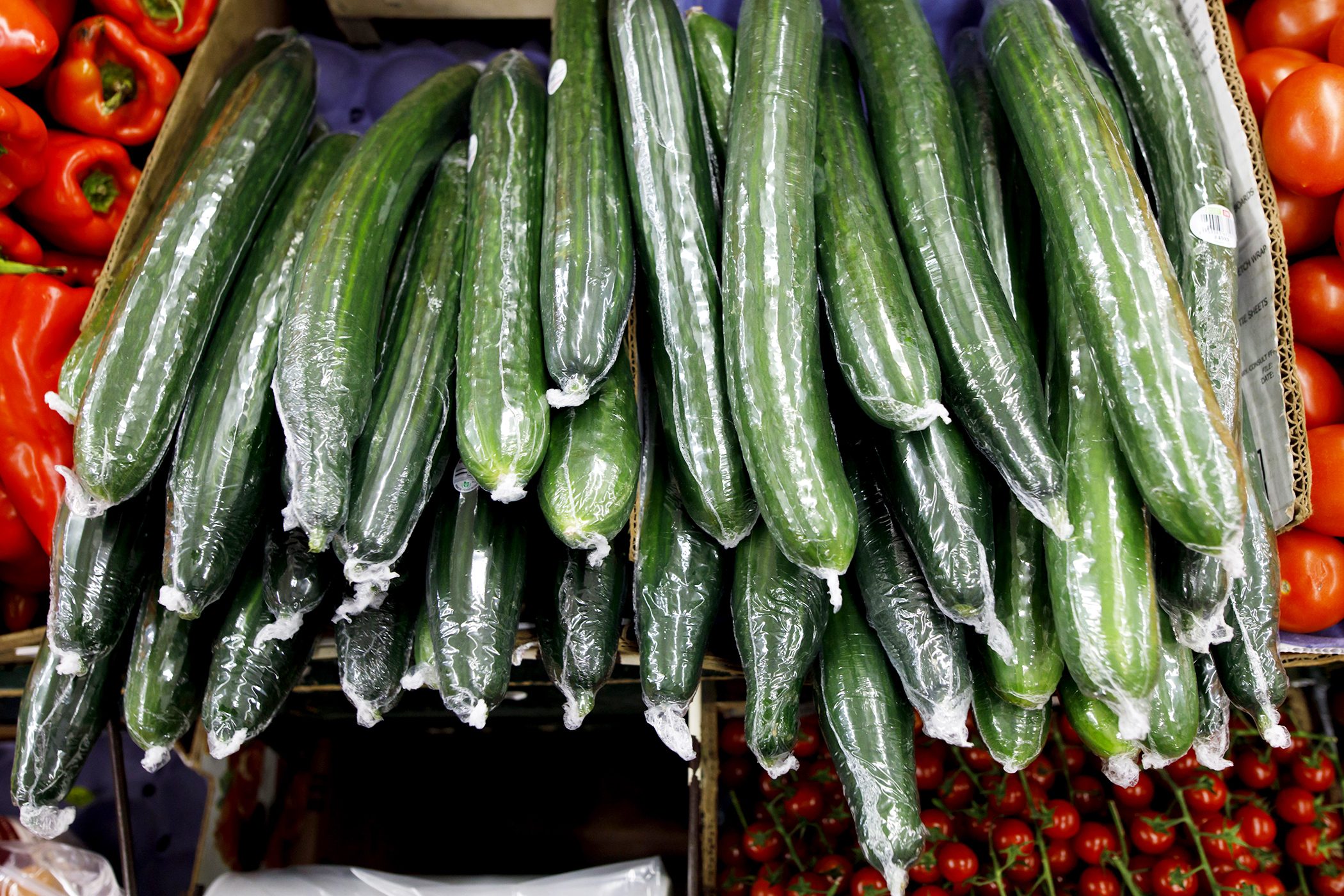 Fresh green cucumbers sit wrapped in plastic film alongside red tomatoes and red peppers in Toronto, Canada. Photographer: Cole Burston/Bloomberg