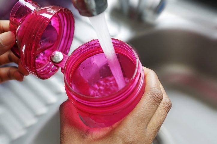 The tap is running with water filling the pink water bottle
