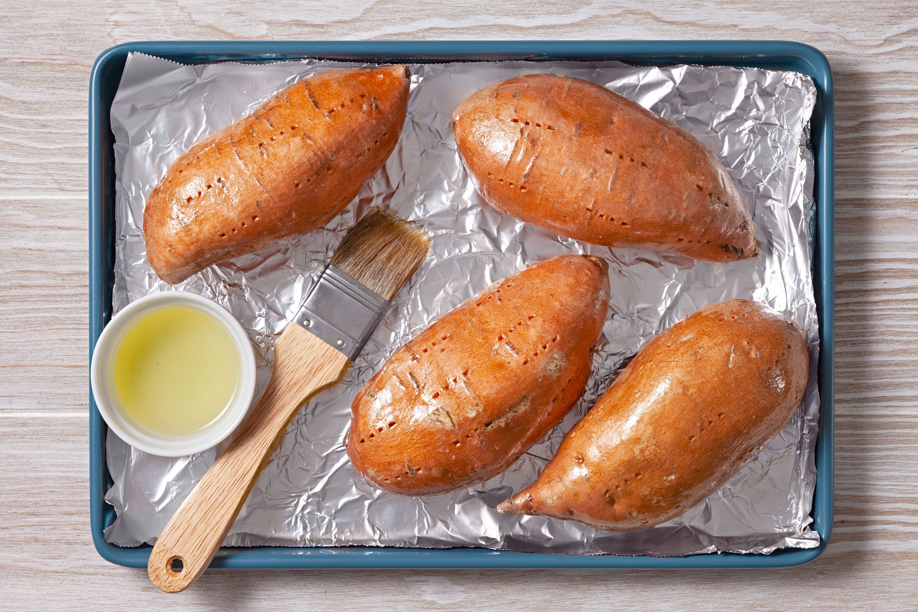 Sweet potatoes on a baking sheet with a brush and oil.