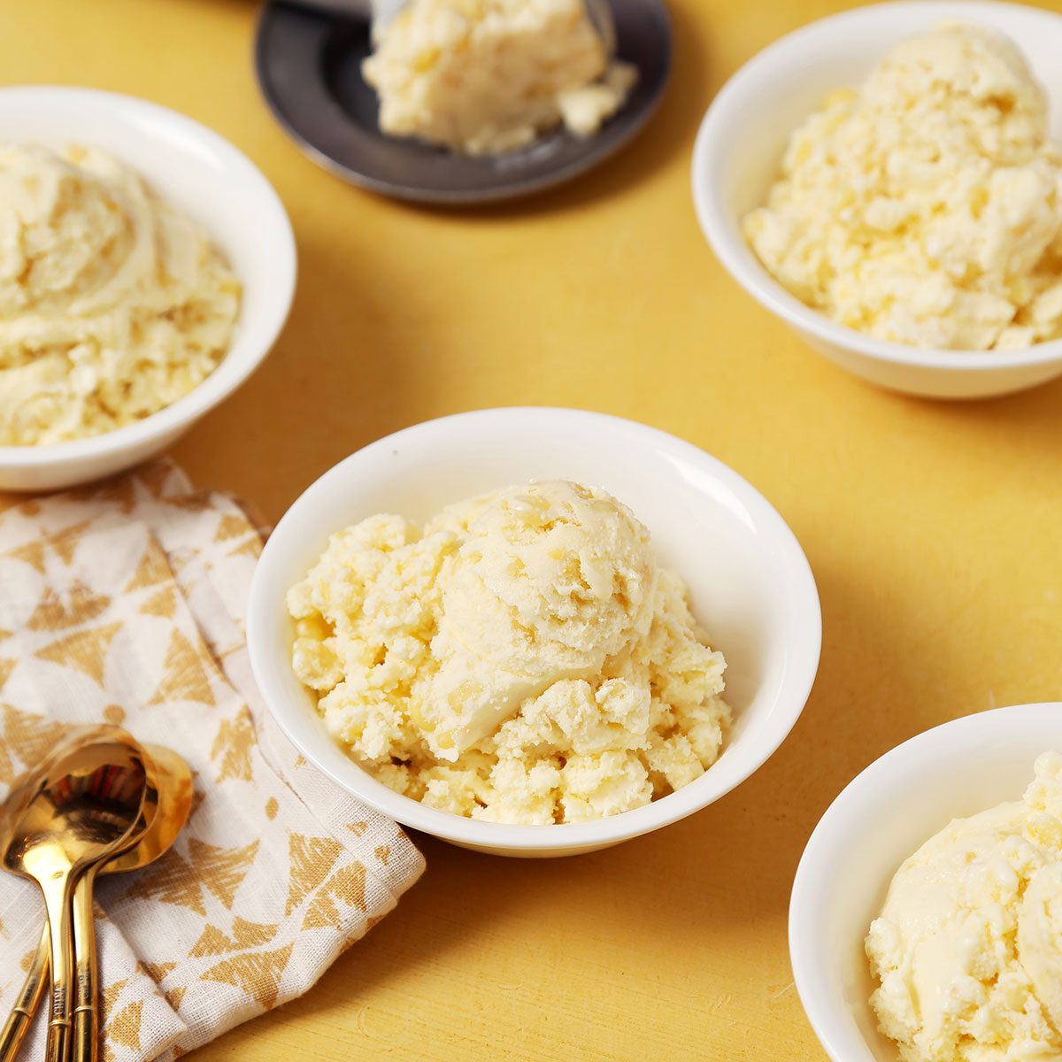 Close up of Taste of Home's Corn Ice Cream scooped and served in small white bowls on a yellow surface.