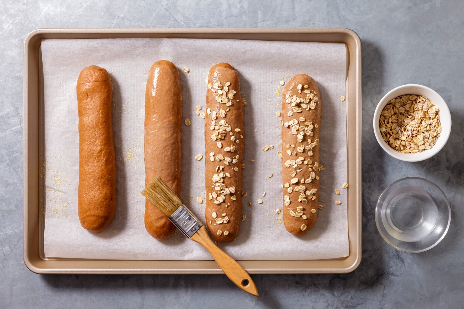 Overhead shot of gently brush the loaves with water; sprinkle lightly with rolled oats; cover loosely with a clean towel; let the dough rise in a warm place until doubled about 1 hour; Meanwhile preheat oven to 350 degree; uncover loaves; bake 25-35 minutes; remove; let cool slightly; brush; grey surface;