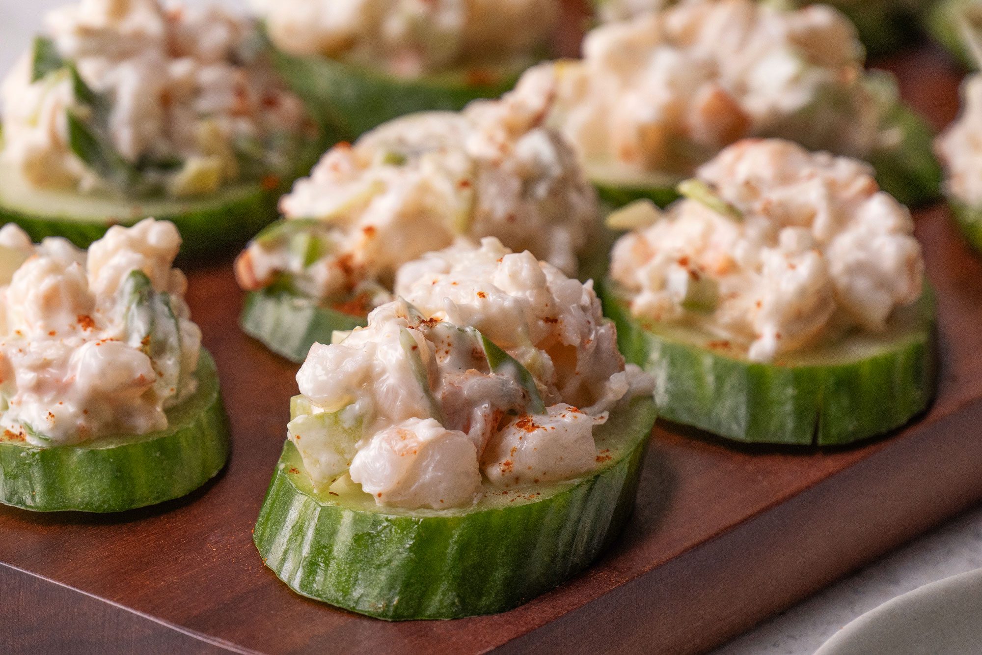 Close-up shot of Shrimp and Cucumber Rounds served on a dark brown wooden tray; set on a marble surface